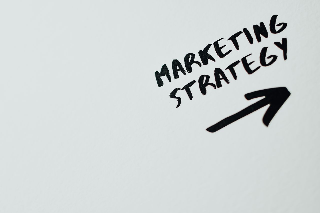 Close-up view of handwritten Marketing Strategy text with an arrow on a white background.
